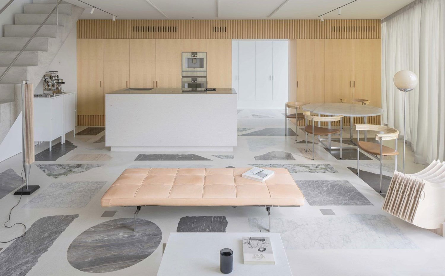 Asiento en capitoné, isla de trabajo en cocina, frente de armarios en madera natural, mesa circular en mármol, sillas con respaldo circular de madera