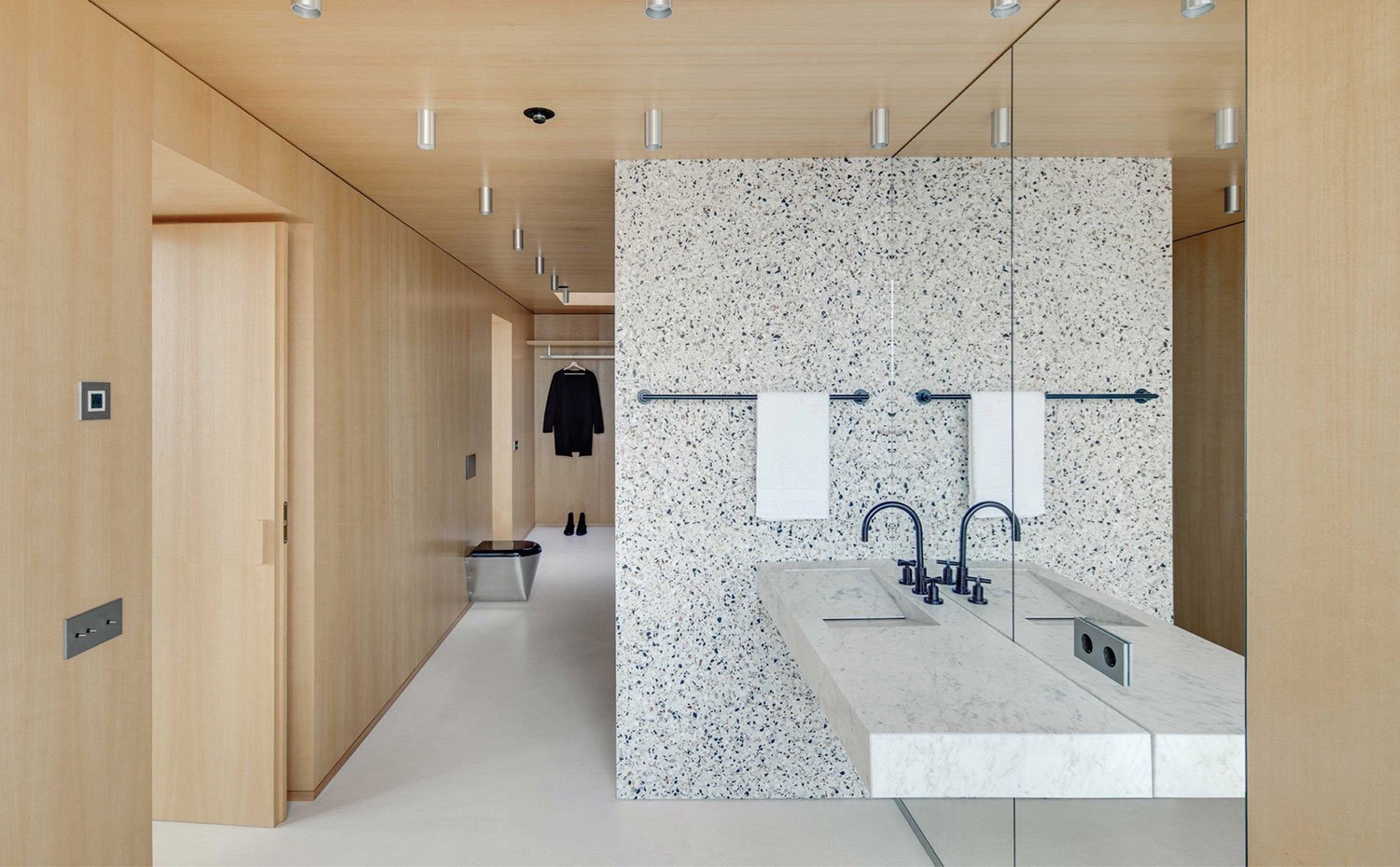 Baño con revestimiento de paredes y techo en madera natural, focos de techo, muro separador de granito, encimera de granito con grifería blanca y espejo de techo a suelo