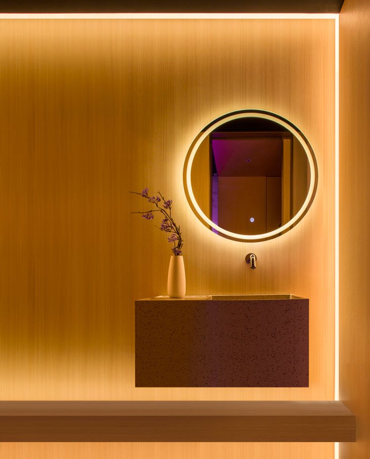 Zona lavamanos baño con revestimiento en amarillo, mueble suspendido, espejo circular con iluminación indirecta