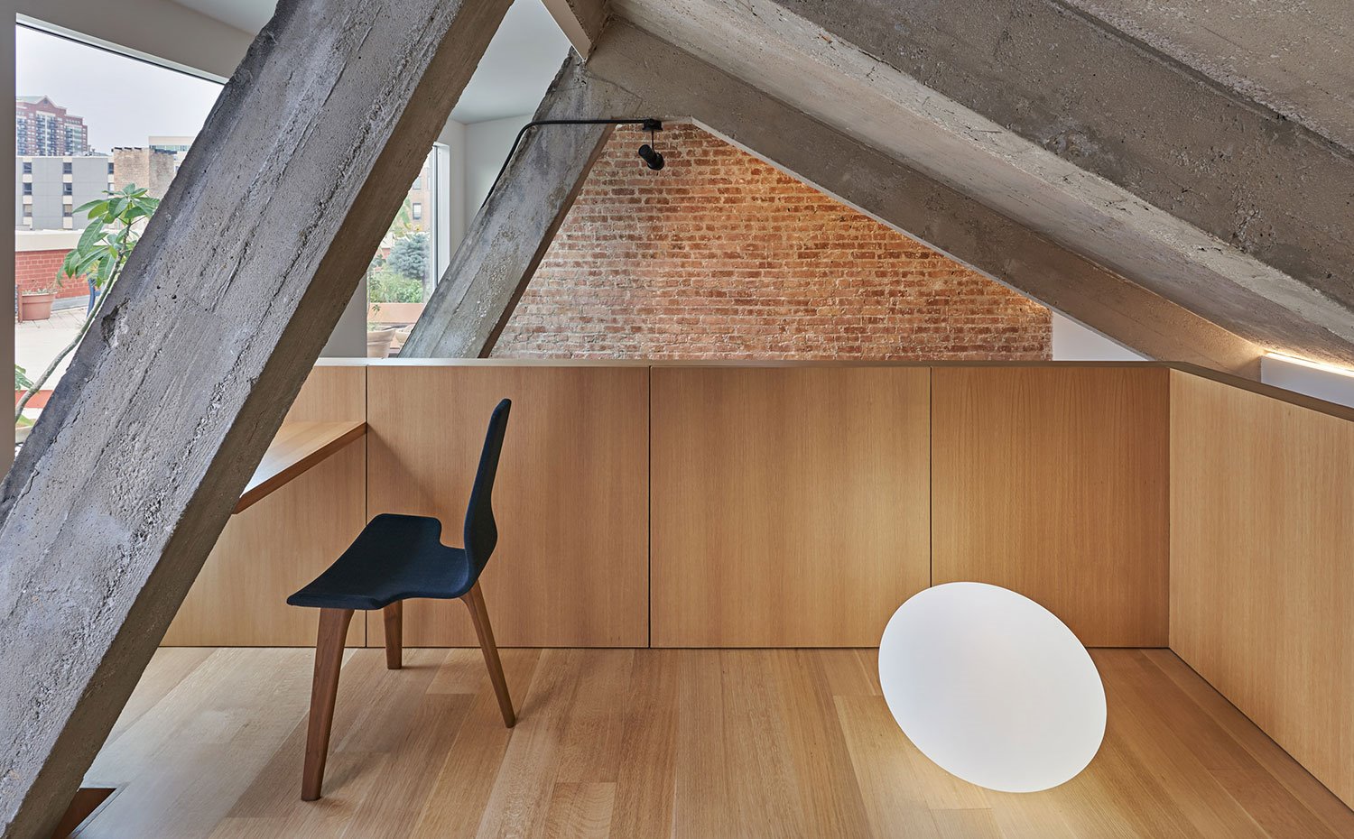 Altillo con suelo de madera, estructura y vigas en hormigón, pared en ladrillo visto, silla de madera en negro, mesa de madera a medida, iluminación suelo con forma circular