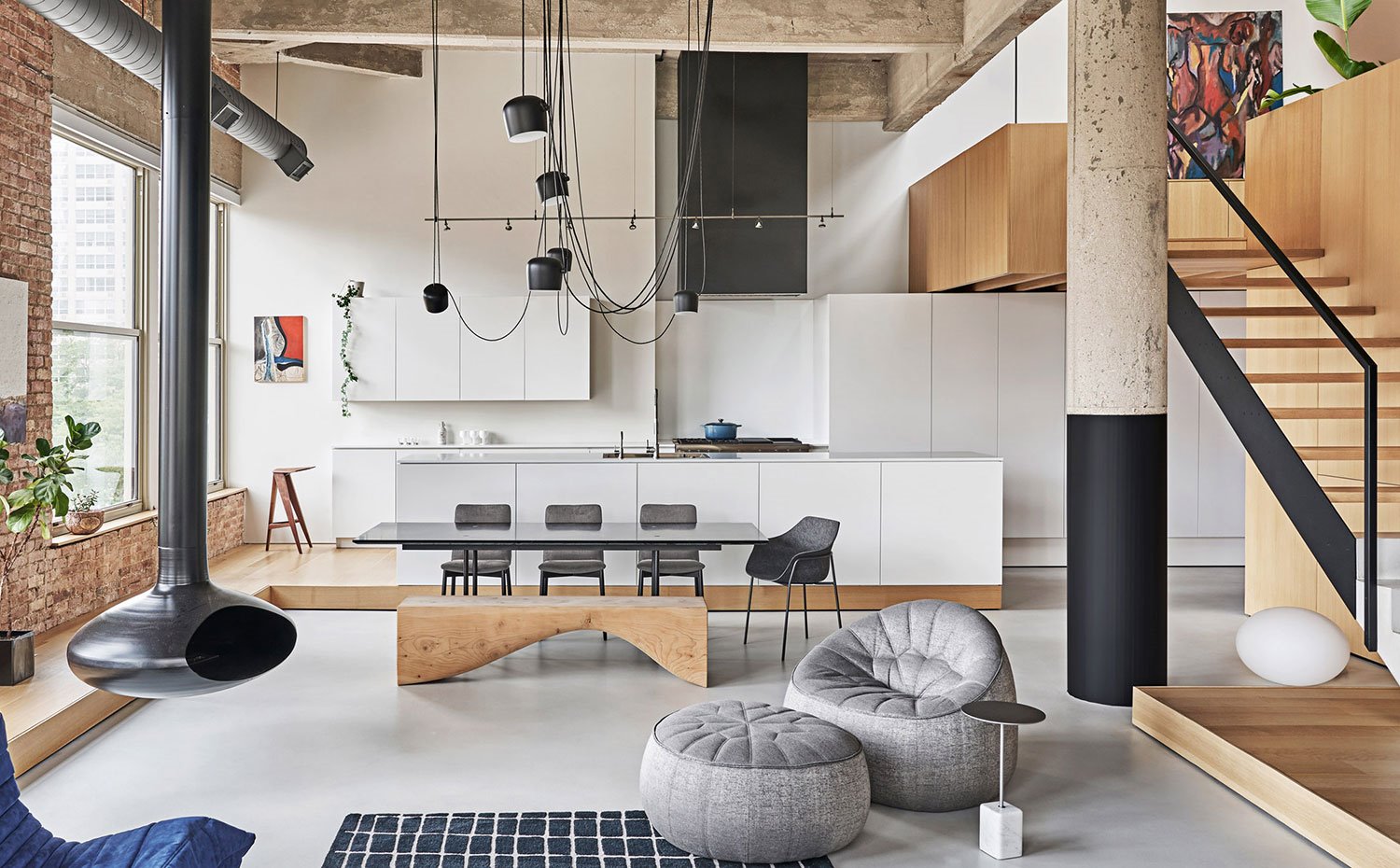 Comedor y cocina junto a salón, sillas en gris, mesa con sobre de cristal, cocina abierta con isla, mobiliario en blanco, campana en engro, revestimientos junto a ventana en ladrillo visto
