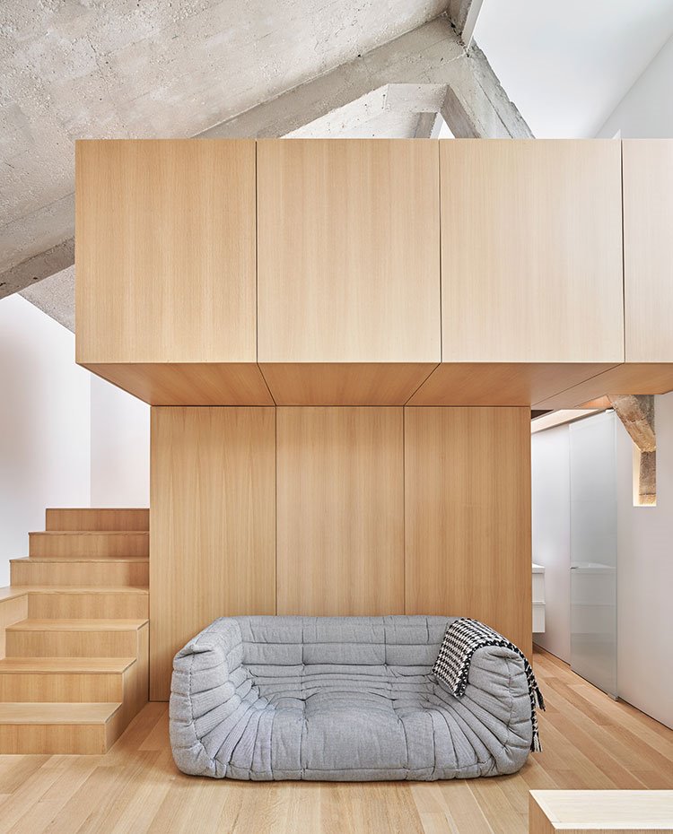 Estructura de madera con escaleras a nivel superior, sofá gris bajo voladizo, suelo de madera