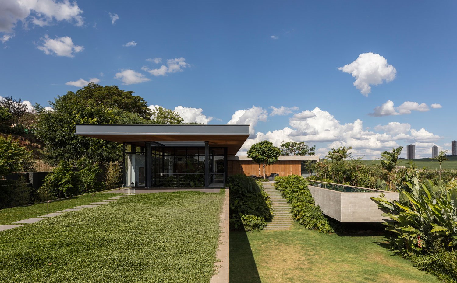 Fachada exterior con jardín junto a puerta de acceso, estructura de cristal, planta en L con terraza exterior y piscina en voladizo