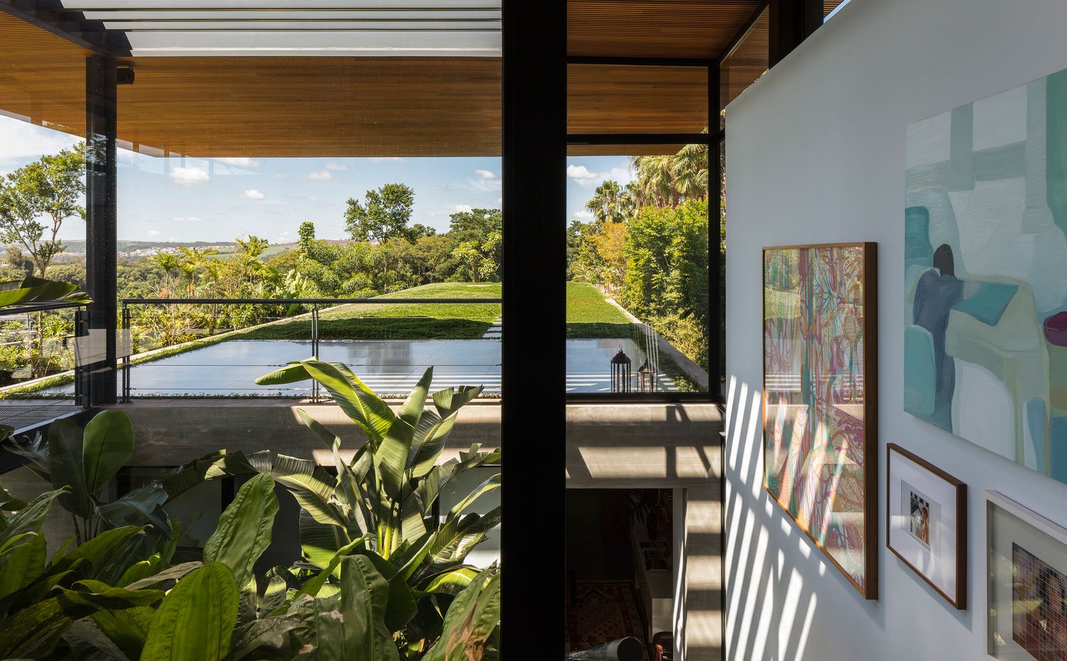 Interior con cuadros de pinturas abstractas, plantas y paisaje frondoso, jardín exterior, bajocubierta de madera