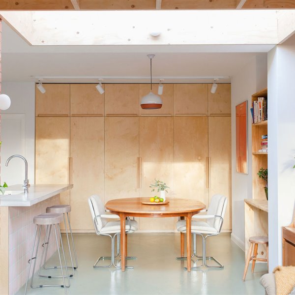 Estantería de madera con plantas, mesa de madera circular, sillas de piel blanca, taburetes grises, armarios de frente madera