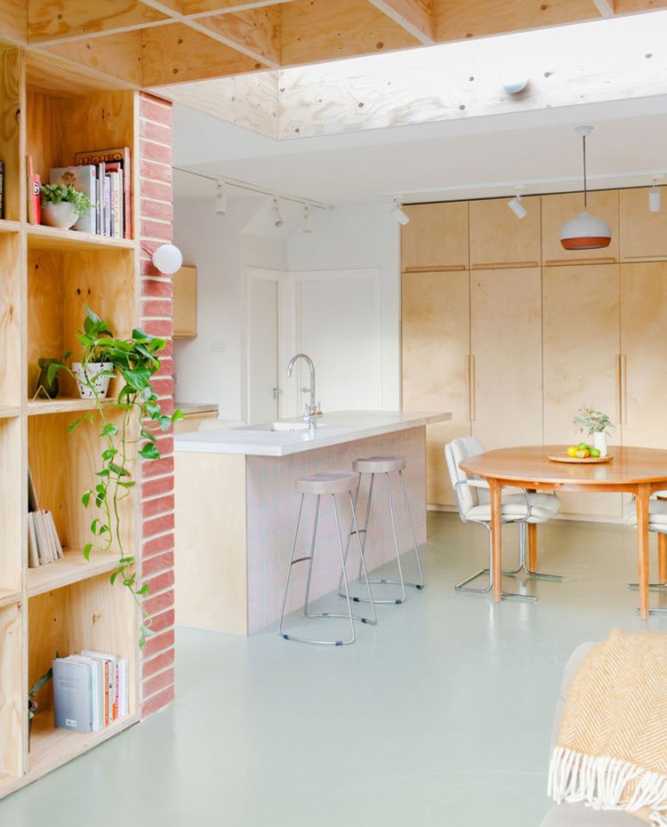 EStructura de madera bajocubierta, librería con macetas y libros, manta en respaldo sofá, isla de cocina con taburetes y mesa comedor en madera