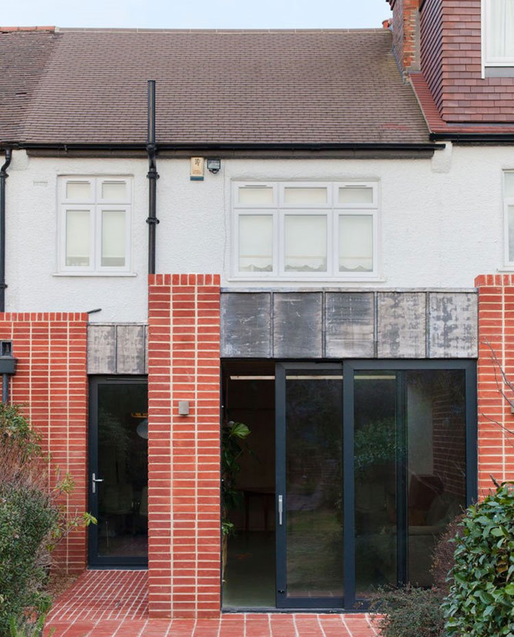 Fachada exterior con cerramientos correderos en aluminio negro y revestimiento de ladrillo visto