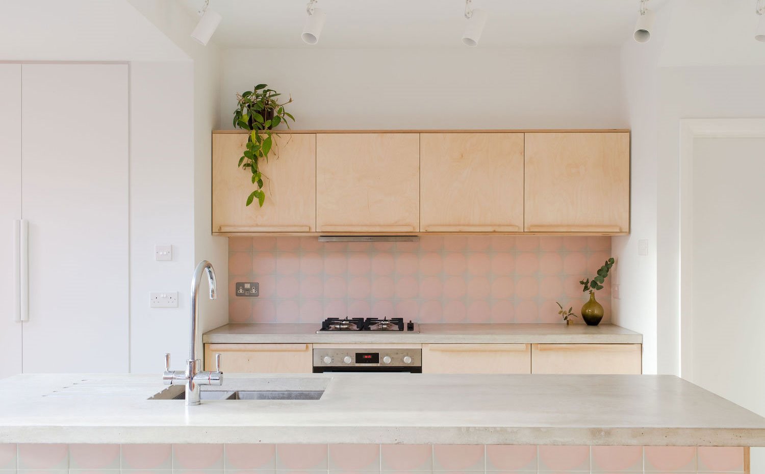 Frentes de cocina en madera clara, revestimientos en gres rosa, encimera de hormgión, armario encastrado en blanco