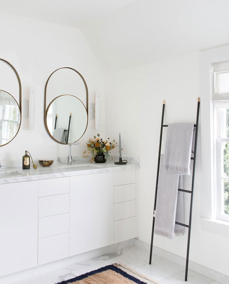 Baño principal con mobiliario blanco, encimera de mármol, espejos redondos, toallas dispuestas en cascada