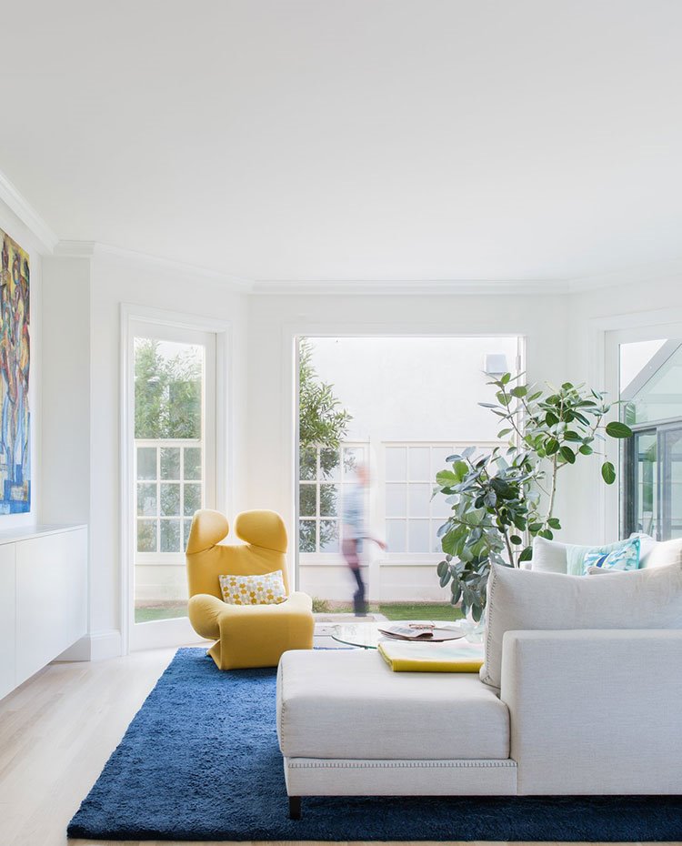 Sala de estar con butaca amarilla, alfombra azul, sofá en L blanco