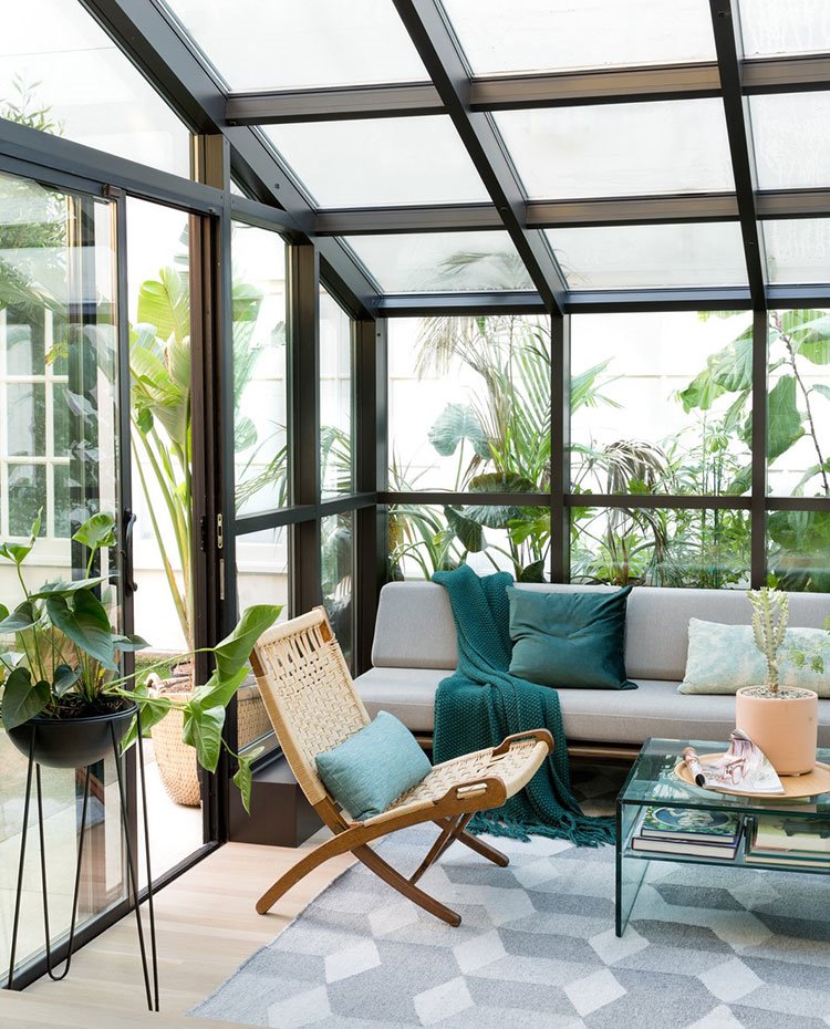 Solarium con soá en gris, mesa auxiliar, butaca de madera y tejido natural, alfombra gris con motivos geométricos, suelo de madera