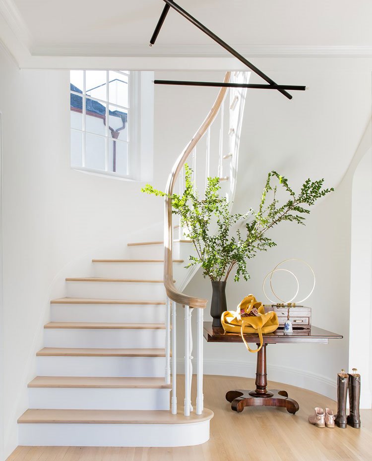 Vestíbulo con escaleras de peldaños de madera, barandilla de madera, con jarrón con flores sobre mesa de madera y lámpara de luz moderna