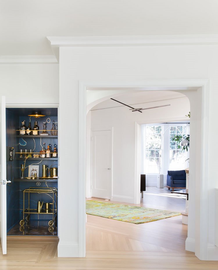 Zona de paso, pavimento de madera, interior puerta mini-bar en azul cobalto, alfombra en verde, sofá azul y iluminación de pie