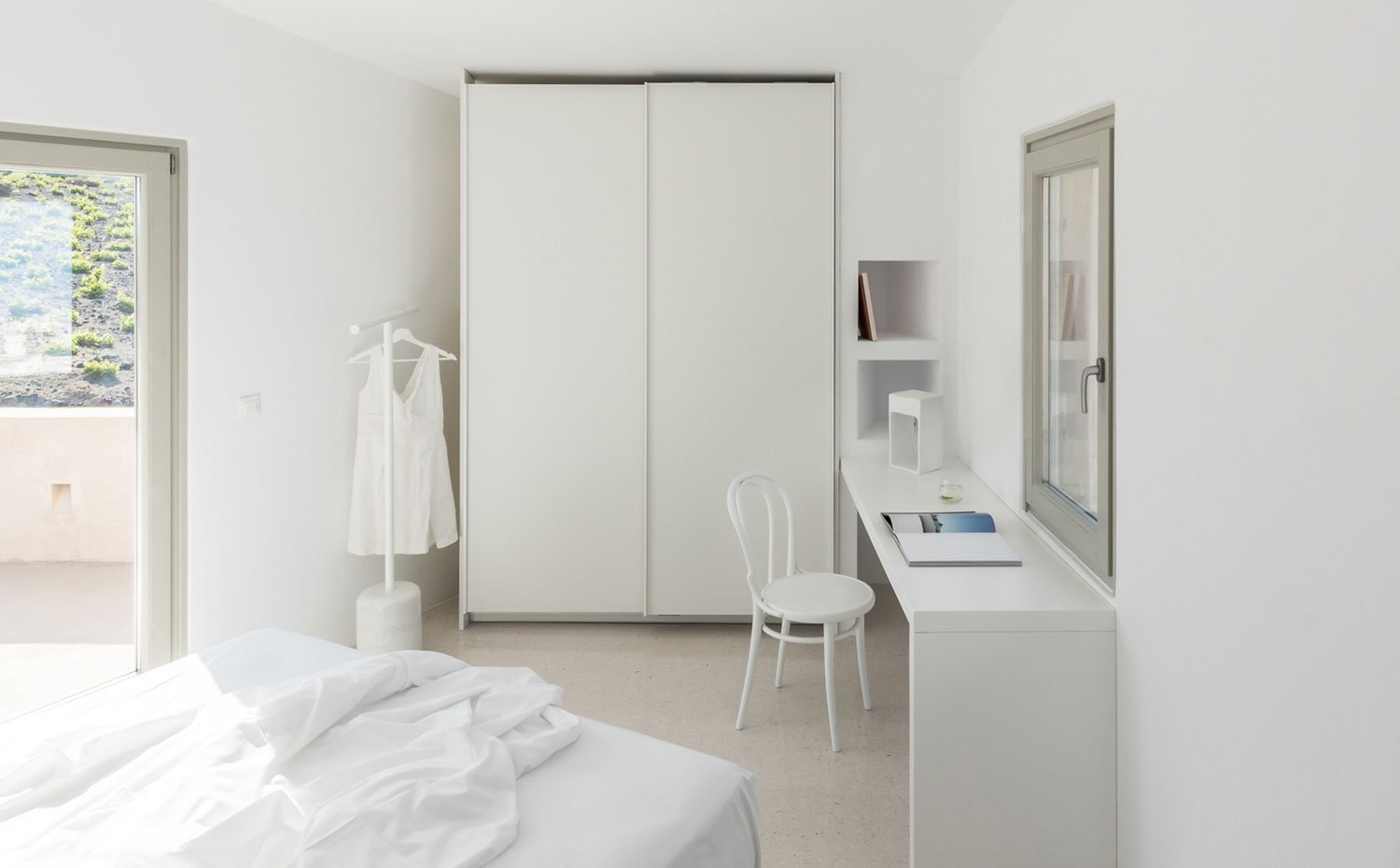 Interior dormitorio con armario corredero, zona de estritorio, colador de pie y cama, todo en blanco