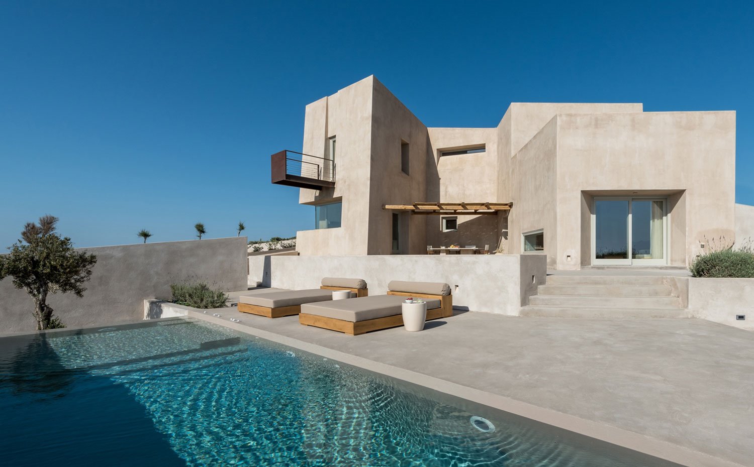 Piscina hecha a medida en hormgión, hamacas con estructura de madera y colchón beige, porche con celosía de madera en hueco entre salientes edificio principal