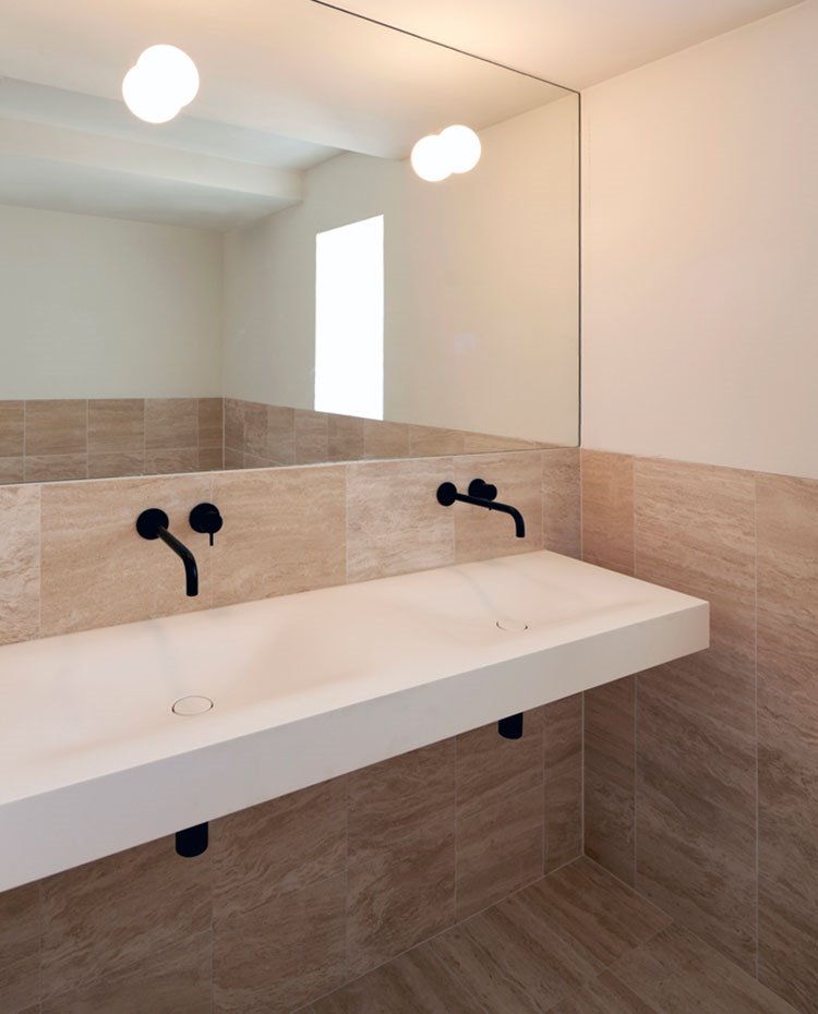 Baño revestimiento porcelánico a media altura, espejo con apliques, lavamanos con doble seno suspendido, grifería empotrada negra