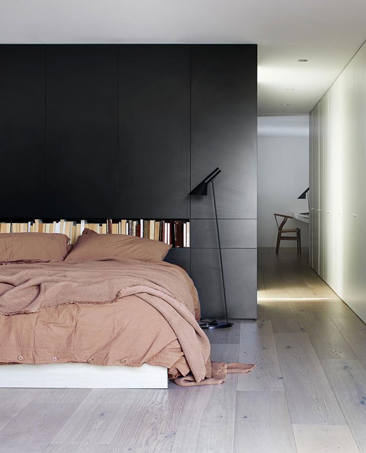 Cama dormitorio con estructura de madera, cabecero con hueco para libros y módulo separador lacado en negro, lámpara de pie negra, suelo de madera