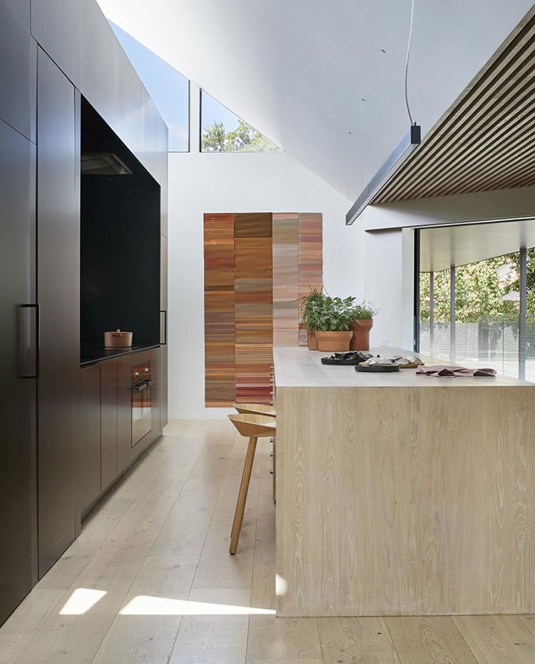 Cocina con isla de office en madera, suelo y taburetes de madera natural, frente de trabajo y almacenaje en negro