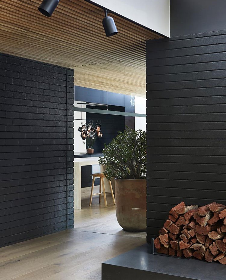 Detalle madera de chimenea, paredes en ladrillo visto en gris antracita, maceta extragrande, taburete de office de cocina, suelo de madera