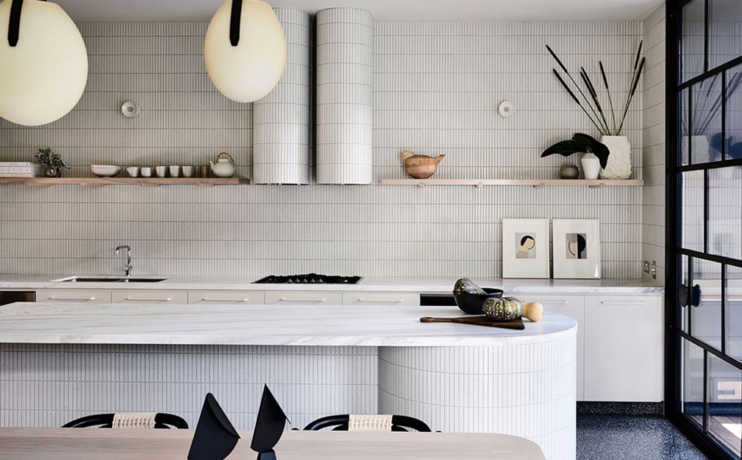 Cocina revestida con baldosas alistonadas, frente de trabajo con balda superior, isla alargada y mesa de comedor de madera