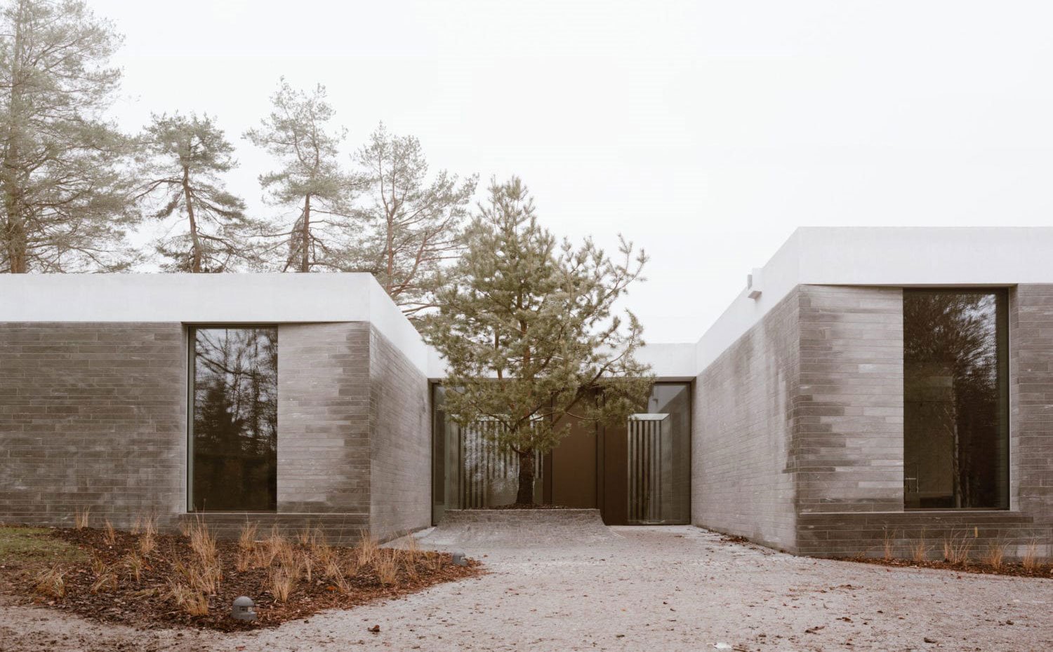 Exterior bucólico de vivienda en forma de U con exterior en gris y blanco y vegetación alrededor