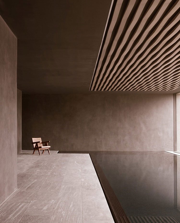 Piscina interior con revestimiento cerámico en suelo y paredes, butaca de madera