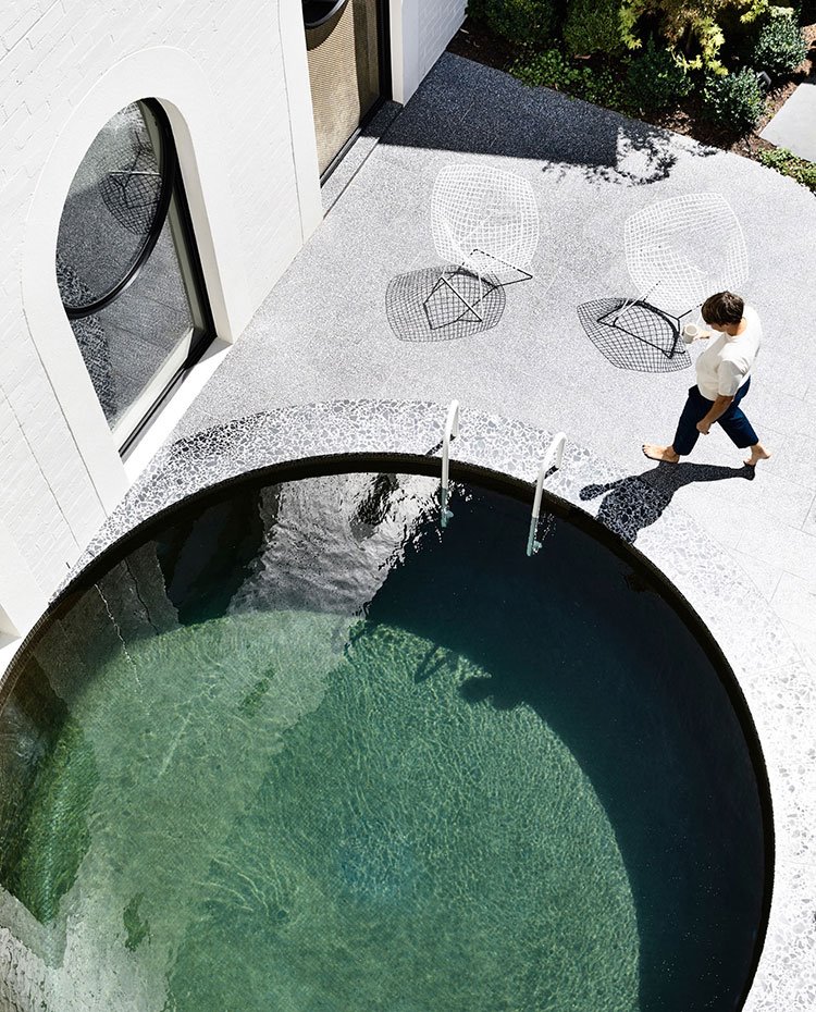 Piscina-redonda-y-verde-junto-a-fachada-principal-edificio,-hombre-andando,-sillas-blancas