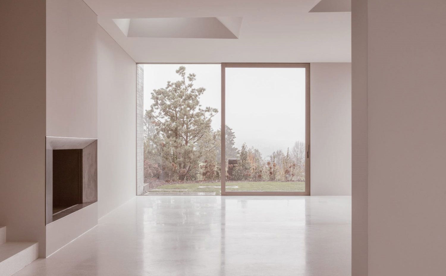 Salón con chimenea con cerramiento corredero a exterior natural, suelo contínuo de hormigón