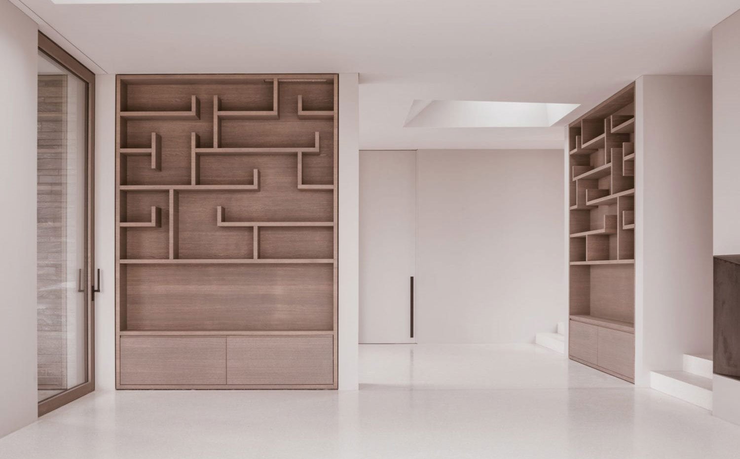Salón con muebles para libros y almacenaje empotrado en dos fretes divisorios, cerramiento de cristal, lucernarios en el techo