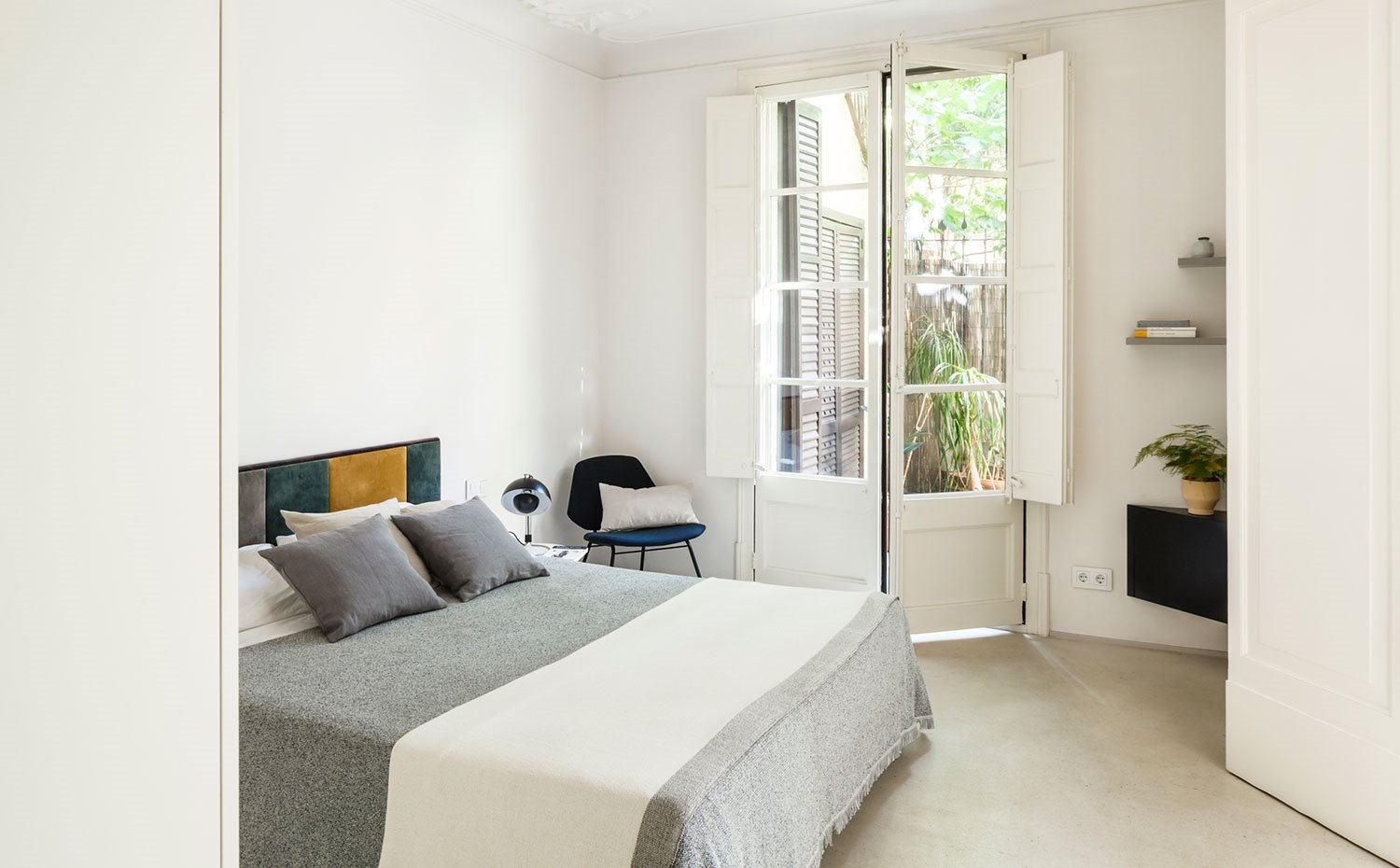 Dormitorio con ropa de cama en gris, cojines en gris, cabecero atercioepelado, butaca en azul oscuro, mueble rinconero