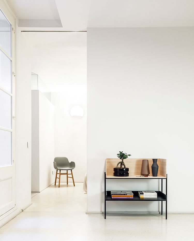 Zona de paso, todo en blanco, mueble auxiliar de madera y acero, bonsai y jarrones decorativos, silla gris con patas de madera