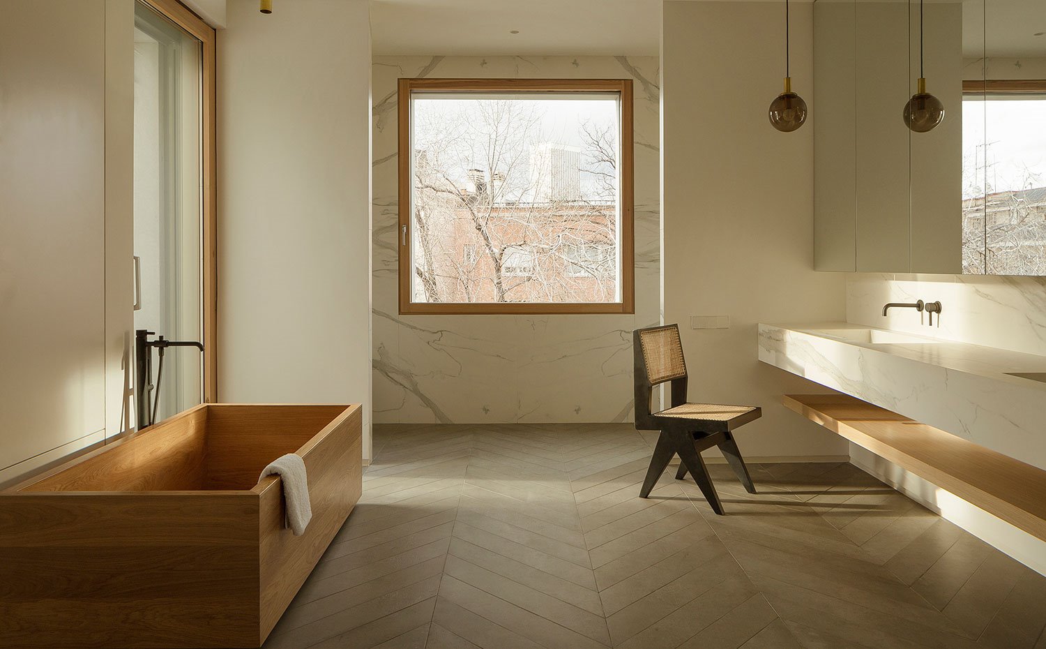 Cuarto de baño con bañera exenta de madera, zona de aguas revestida de mármol, zona de lavamanos con estructura de piedra de doble seno, mueble suspendido con frente de espejo y blanda inferior madera