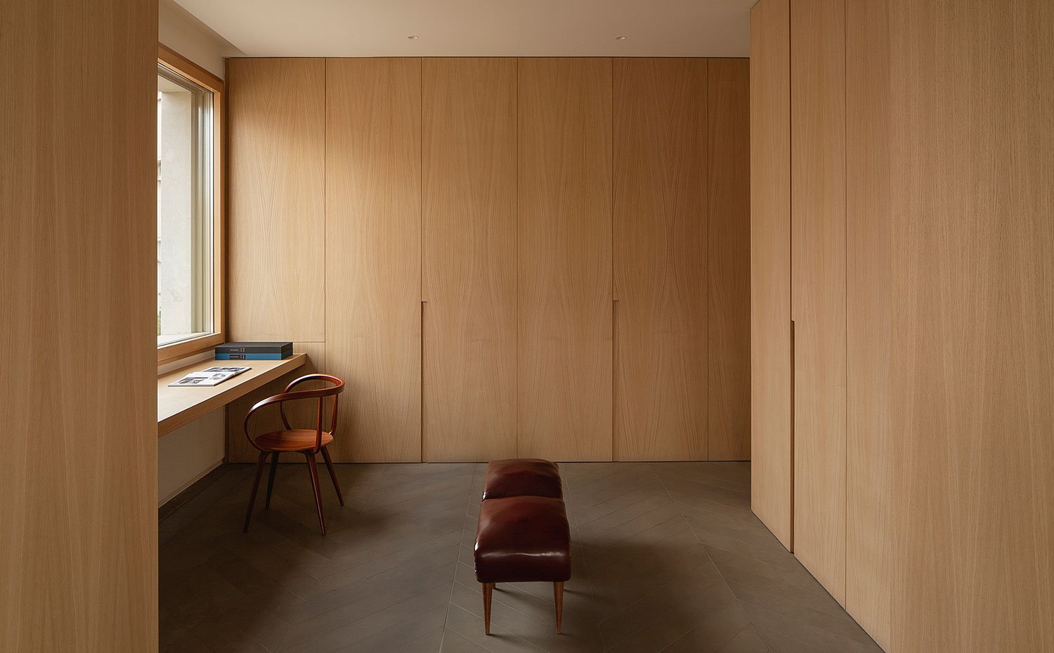 Zona de trabajo y almacenaje con serie de armarios con tirador integrado, bancada de madera y piel, silla de madera.