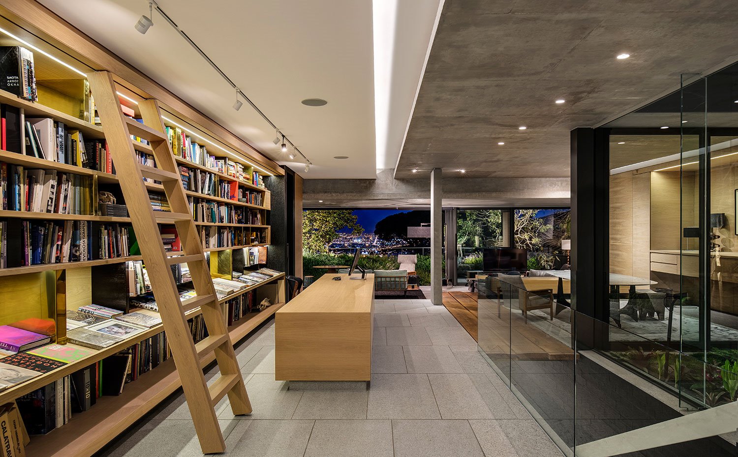Biblioteca con escalera de madera, mueble almacenaje central de madera, zona de estar al fondo, con vistas al exterior
