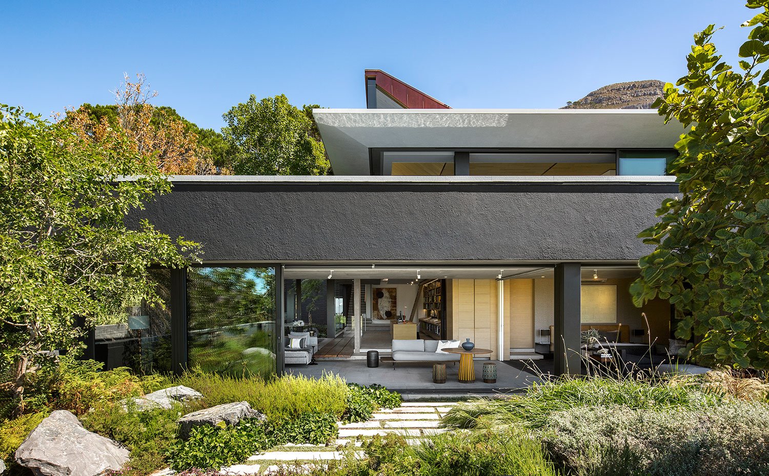 Exterior vivienda a jardín con salón abierto, camino de piedra, cerramientos de cristal