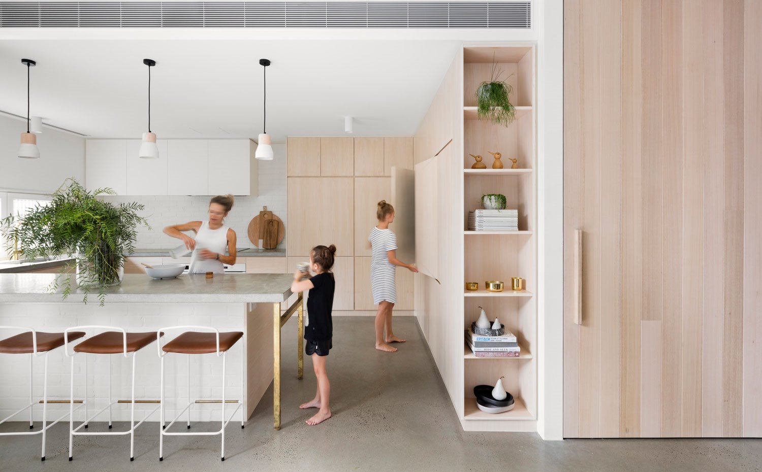 Cocina abierta, taburetes blancos con asiento marrón, muebles de madera, encimera gris, tres luminarias suspendidas