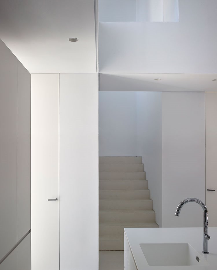Detalle hueco escalera junto a zona de aguas de cocina, todo en blanco con iluminación encastrada en bajo techo