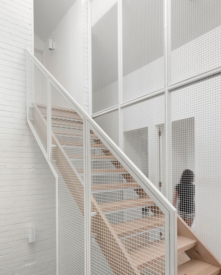 Escaleras hacia nivel superior, pared de ladrillo visto pintado blanco, escalera de madera ocn estructura a modo de rejilla