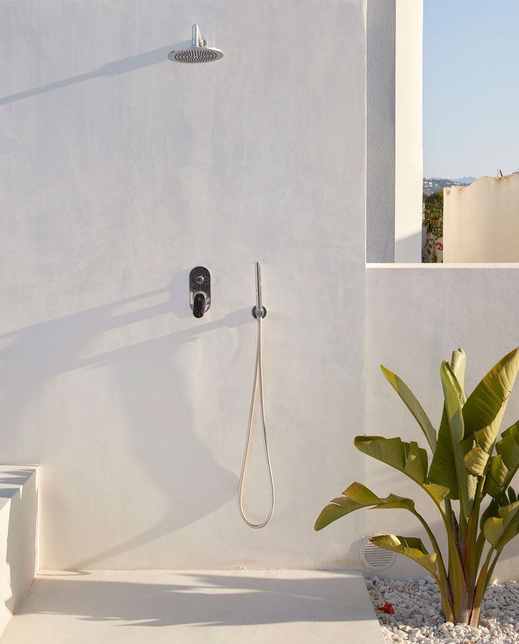 Ducha exterior junto a piscina sobre pared encalada blanca y piedra de canto rodado