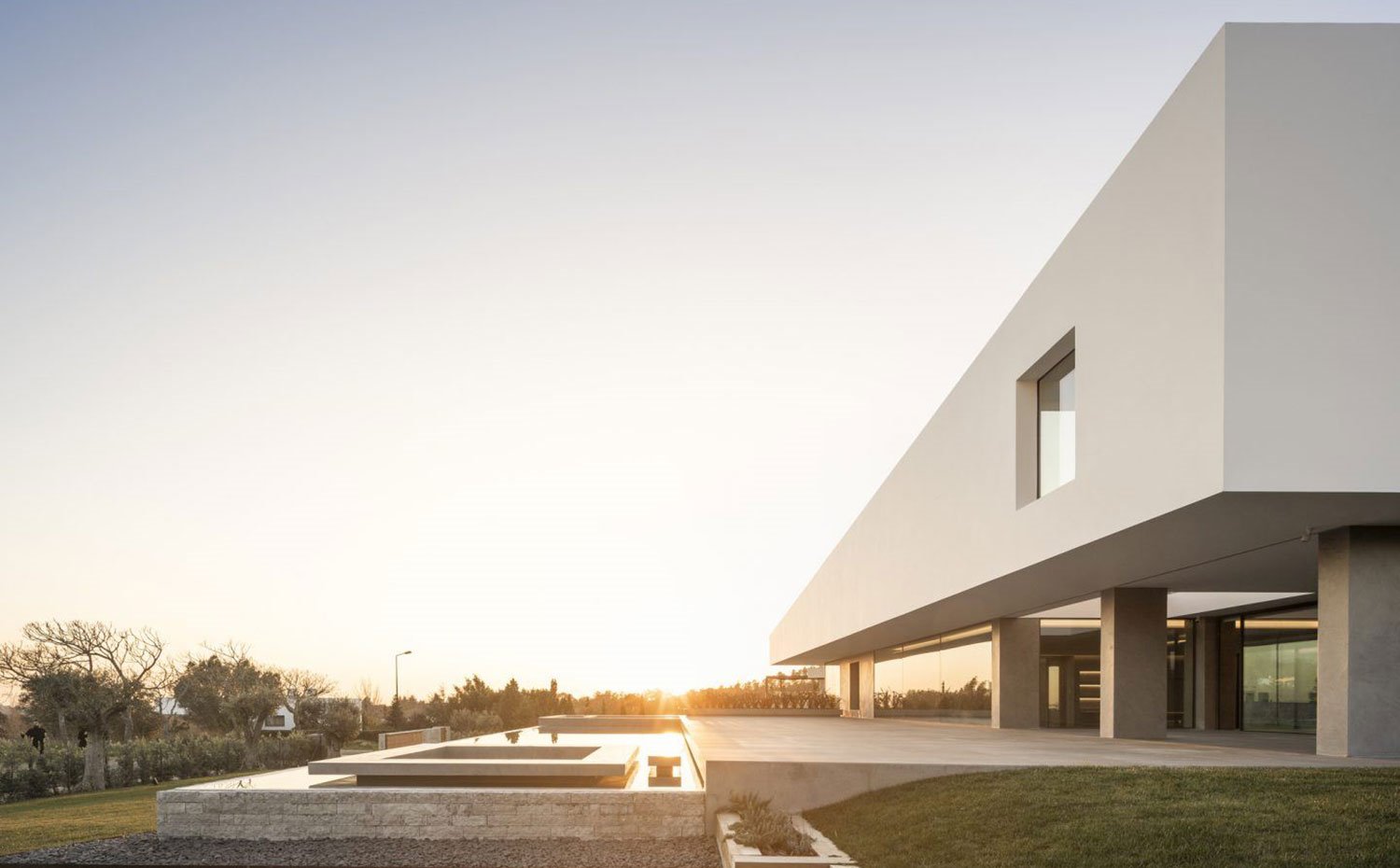 Exterior vivienda al atardecer con piscina infinita en la parte baja del porche, junto a zona ajardinada
