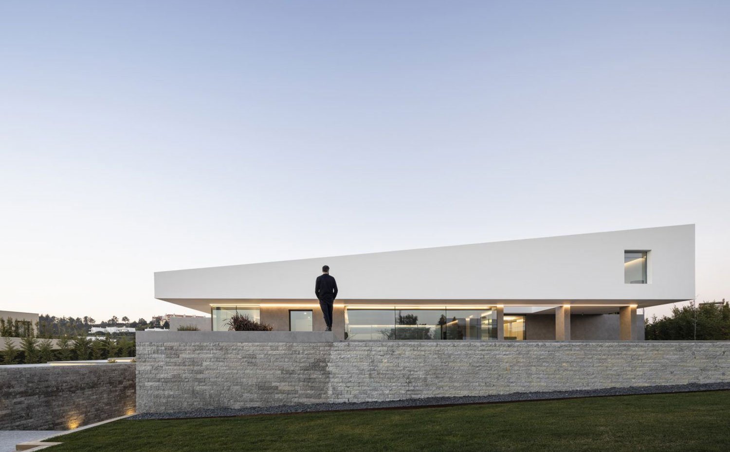 Fachada exterior con muro de ladrillo, fachada de cristal y cerramiento en blanco con techo inclinado hacia zona piscina