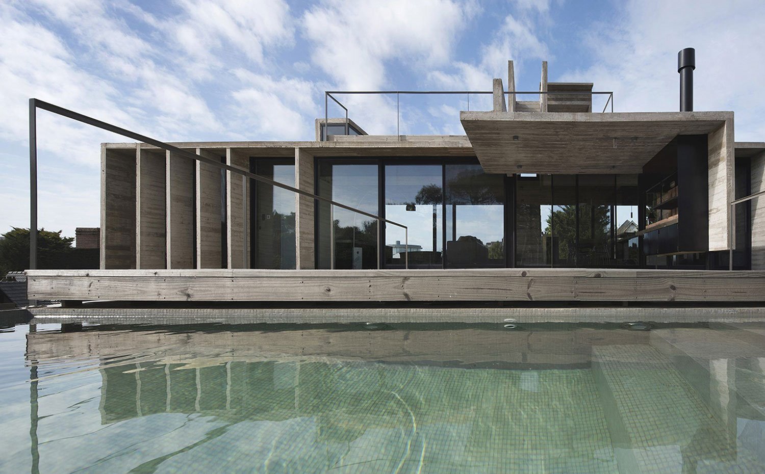 Piscina junto a vivienda, estructura de hormigón, plataforma de madera, cerramientos de cristal