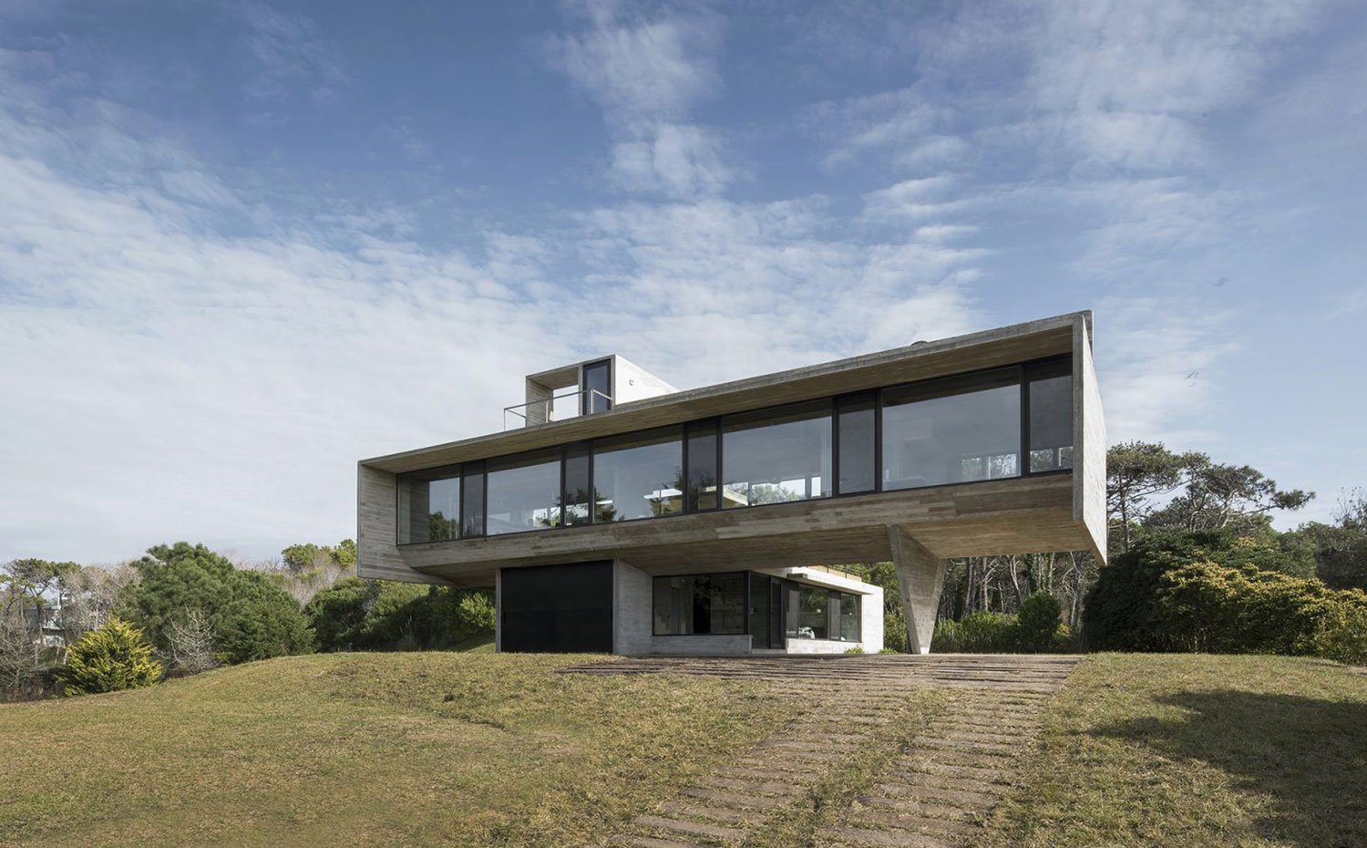 Vista exterior vivienda sobre zona ajardinada, primera planta en voladizo sobre base rectangular