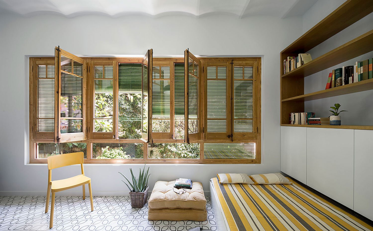 Zona lectura, puf y silla amarilla, mueble almacenaje en blanco y madera, ventanas con perfilería de madera natural a exterior