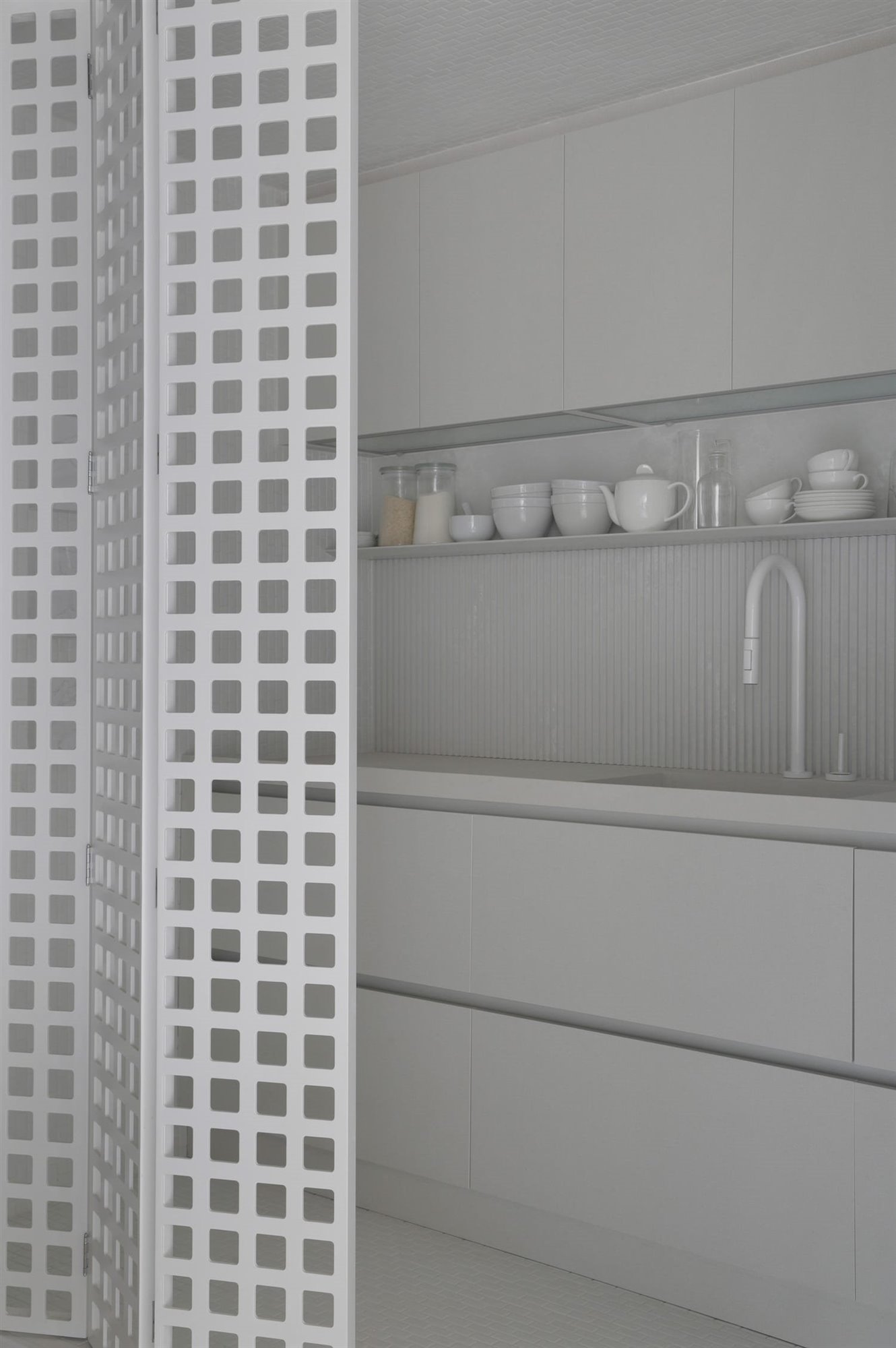 Detalle interior módulo cocina con puerta plegable perforada con motivos cuadrados, encimera, zona de aguas, estantes y amarios