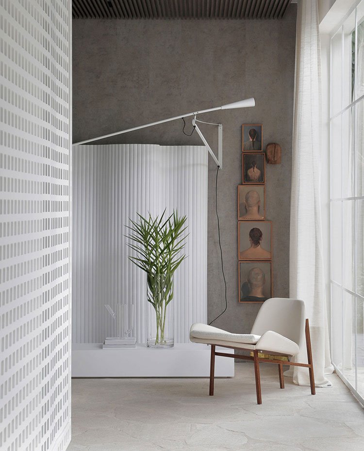 Rincón lectura con butaca en blanco y madera, aplique de pared en blanco a juego con biombo y mueble bajo, revestimiento de hormigón y piedra