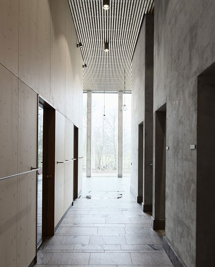 Zona de paso a salas de masaje y tratamiento con revestimiento de hormigón y madera y puertas de cristal
