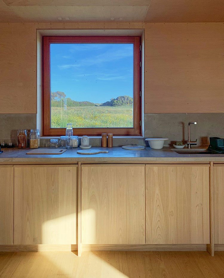 Detalle cocina con mobiliario de madera, sobre de granito gris y apertura al paisaje natural exterior