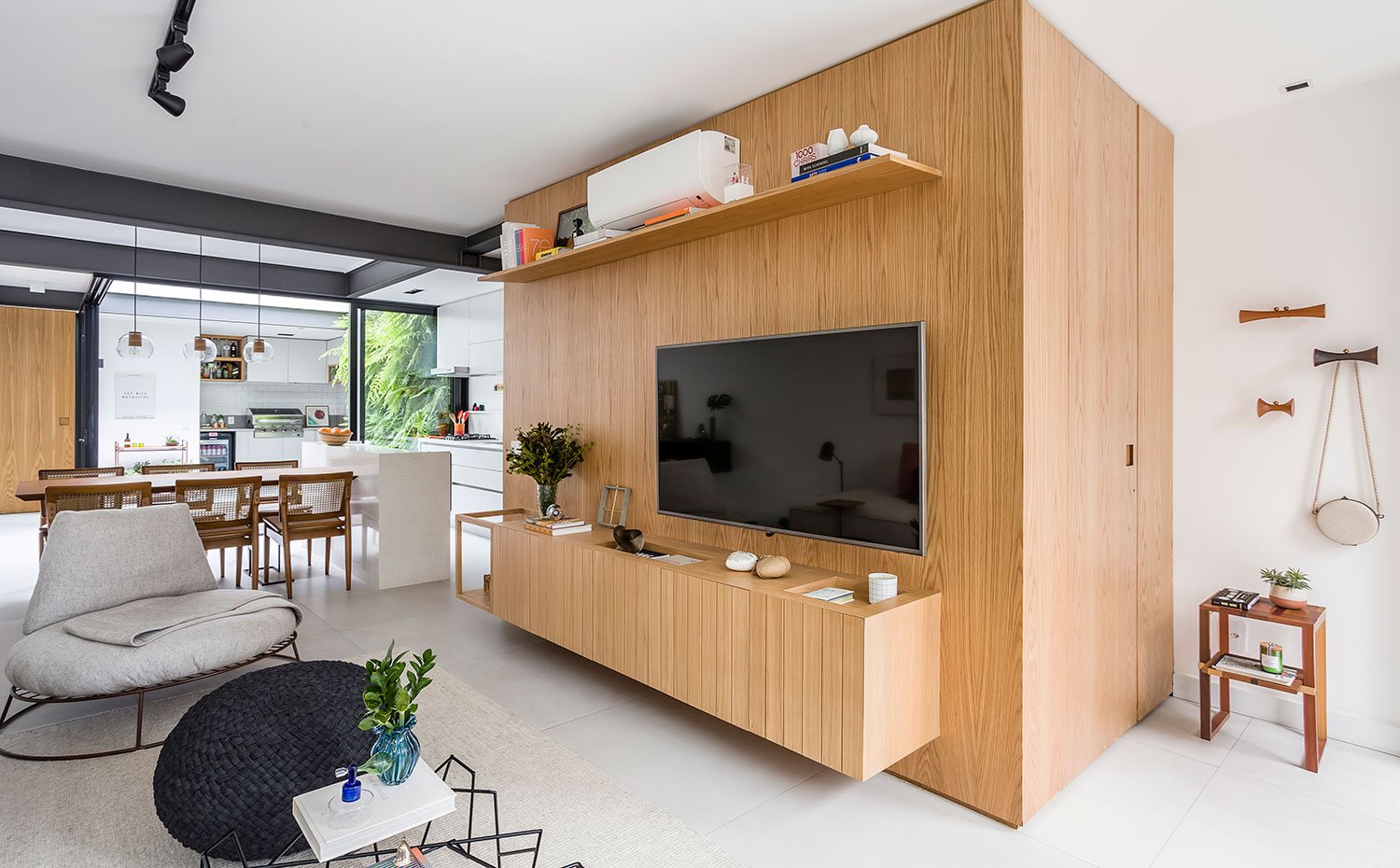 Estructura de madera en salón con módulo bajo TV suspendido y balda superior, junto a comedor y cocina abierta
