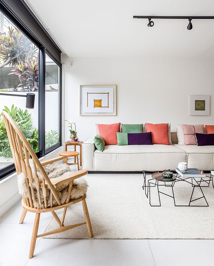 Salón con sofá crudo y cojines de colores, butaca de madera estilo rústico, taburete y mesita auxiliar de madera, alfombra en crudo